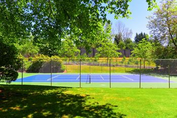 A tennis court is surrounded by trees and a fence at Woodlake Apartments, Washington